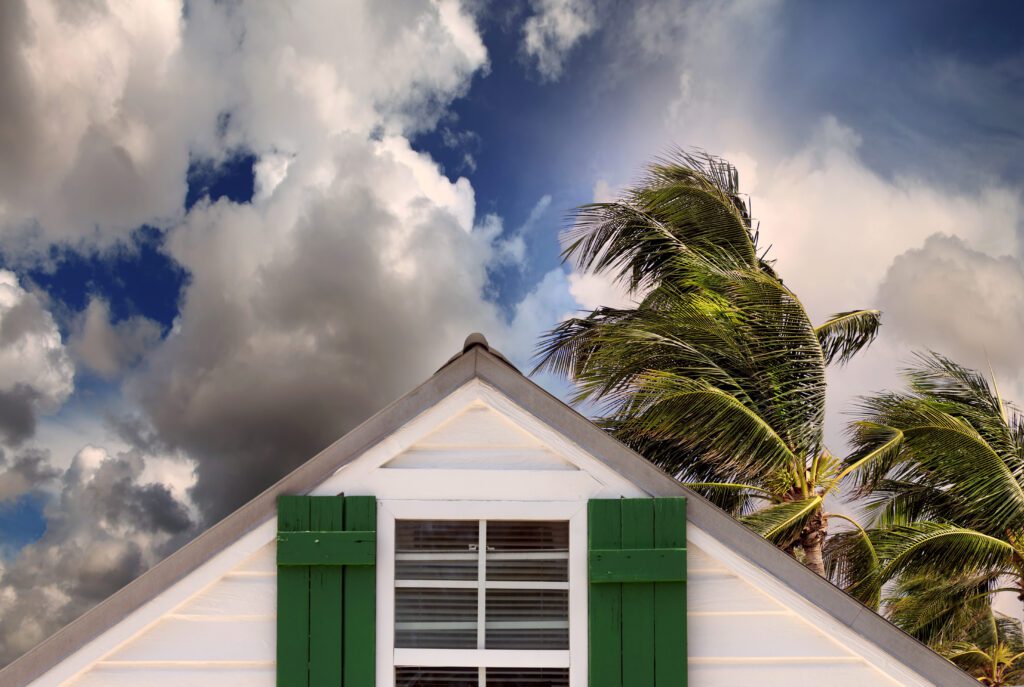 close up rooftop of a wooden house over stormy clouds sky and waving palm tree leaves