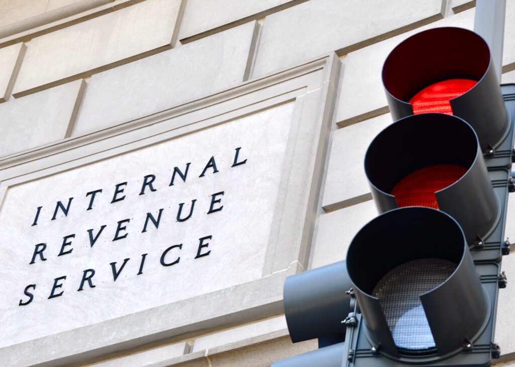 Internal Revenue Service sign with a traffic signal in the foreground indicating a red light.CIC Services to Fight on to See Micro Captives Disclosure Requirement Binned Published by Captive International