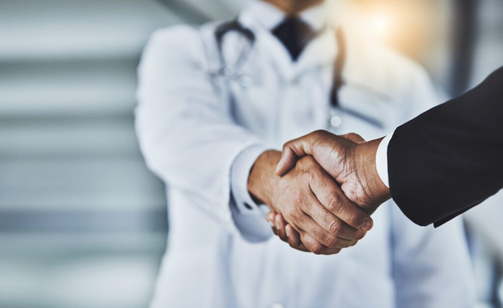 Cropped shot of a doctor shaking hands with a businessman in a hospital - captive insurance