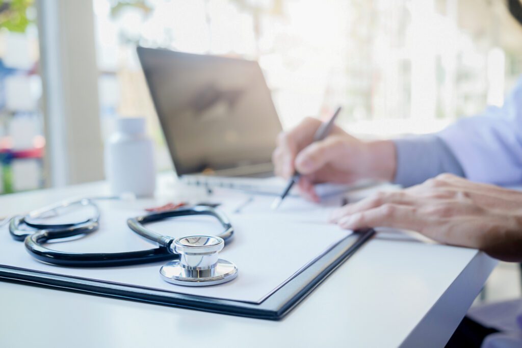 Stethoscope with clipboard and Laptop on desk,Doctor working in hospital writing a prescription, Healthcare and medical concept, test results in background, vintage color, selective focus.